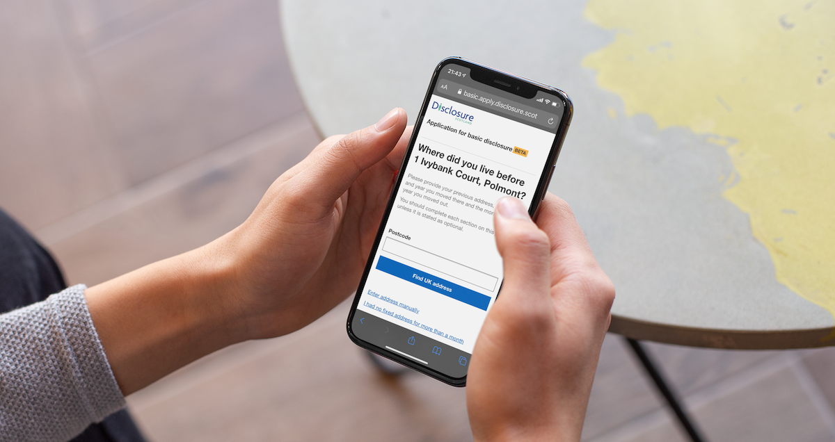 A person holding a mobile phone with the Apply for a basic disclosure service on screen.